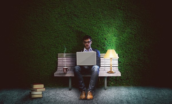 Hombre con portatil, taza y lampara en un banco delante de jardin vertical